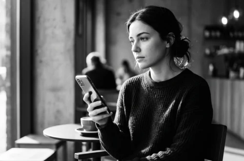 Woman sitting in a cafe, looking at her smartphone with a coffee cup on the table beside her.