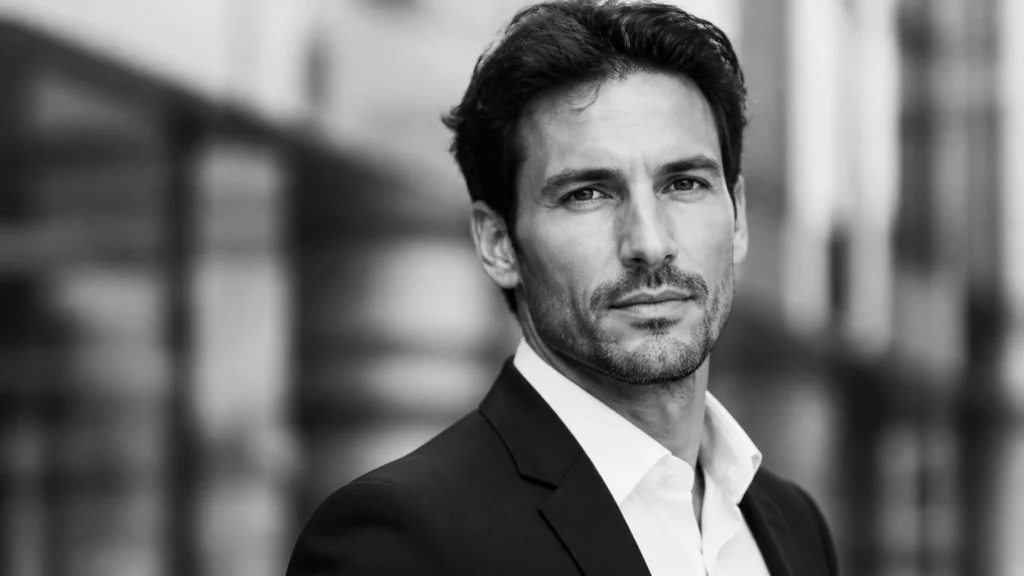 Black-and-white head-and-shoulders portrait of a man in a suit looking at the camera outdoors.