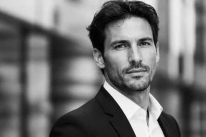 Black-and-white head-and-shoulders portrait of a man in a suit looking at the camera outdoors.