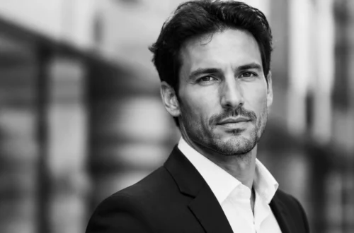 Black-and-white head-and-shoulders portrait of a man in a suit looking at the camera outdoors.