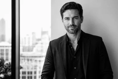Professional portrait of a man in a black suit posing in a modern office with a city skyline in the background (black & white)